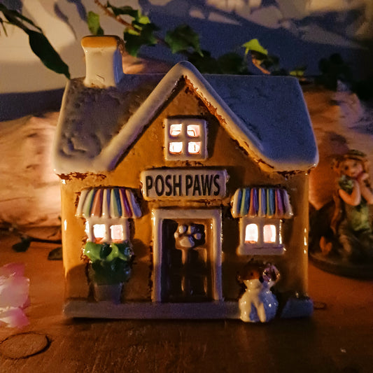 A gentle glow shines from Posh Paws, where tiny windows flicker with warmth as if welcoming beloved companions into a magical village haven. This Shudehill Village Pottery tealight house is crafted from ceramic, allowing candlelight to dance softly through its details, creating a comforting and enchanted atmosphere.