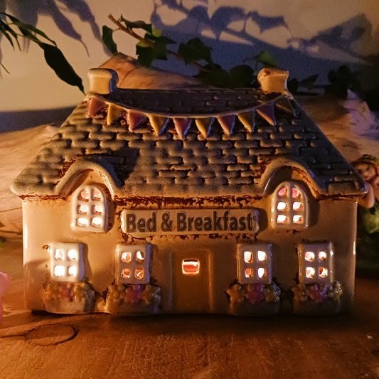 A welcoming glow awaits within this Village Pottery Bed & Breakfast Tealight House, where candlelight flickers through tiny windows like a hearth lit for wandering souls. Crafted from ceramic, this charming inn captures the spirit of an enchanted village, inviting warmth, stillness, and quiet magic into your space.