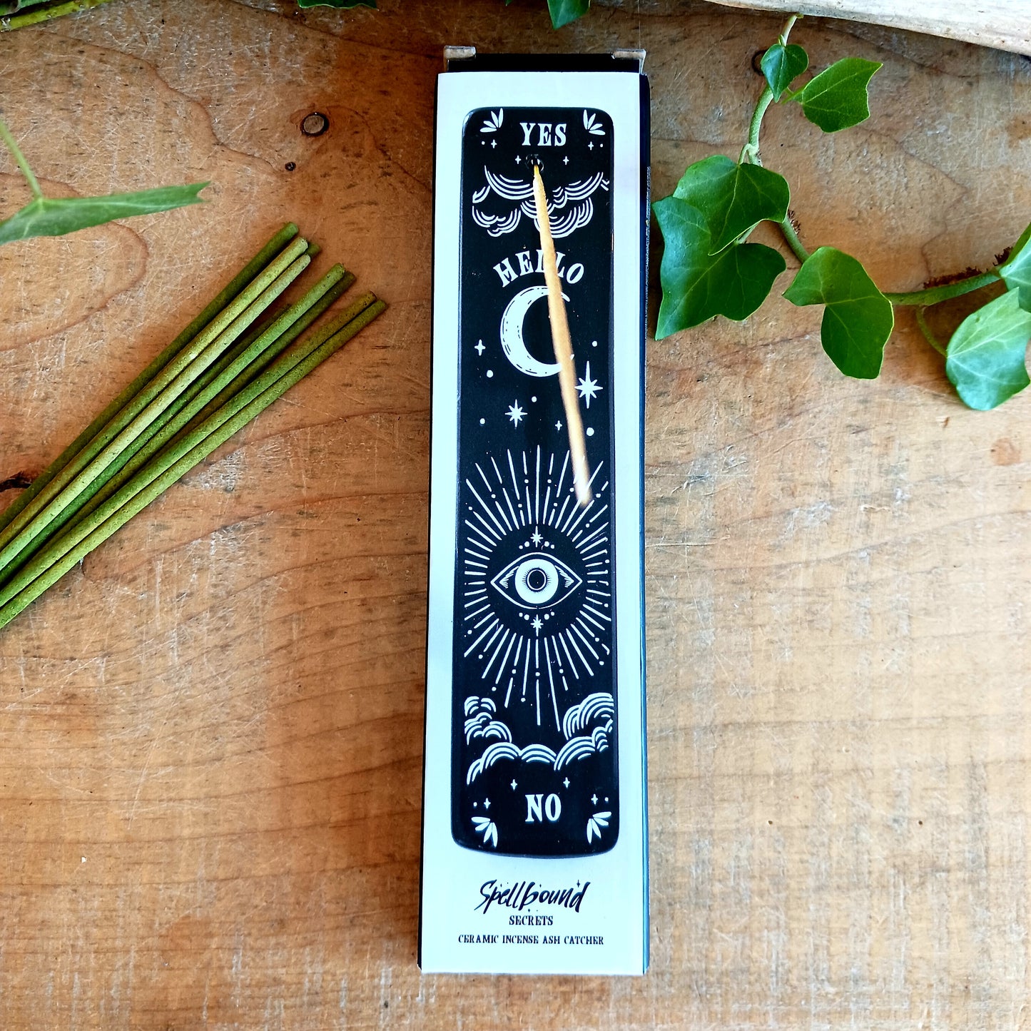 Add a touch of mystical gothic style to your incense rituals with this striking black incense ash catcher, inspired by traditional talking boards. Featuring a decorative planchette-style design surrounded by stars, moons and an all-seeing eye, it creates an atmospheric setting for burning your favourite incense sticks.