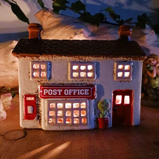 Whispers travel by candlelight from this Village Pottery Post Office tealight house, where tiny windows glow like messages carried between realms. Crafted from ceramic and measuring 12x15x7cm, this enchanting piece brings warmth and quiet magic to your sacred space.