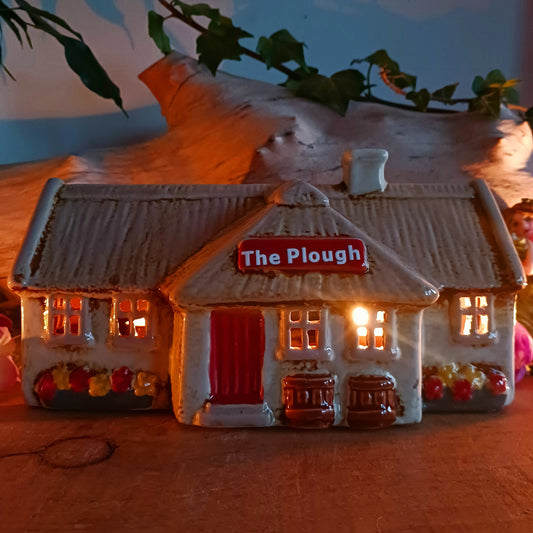 A hearth-lit gathering place where candlelight flickers like laughter carried on the evening air, the Croft Plough Pub brings rustic enchantment to your village scene. This Shudehill Village Pottery tealight house is crafted from ceramic, casting a warm, inviting glow through its windows to evoke comfort, connection, and quiet magic.
