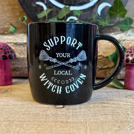 Show your support for all things magical with this black ceramic mug featuring crossed broomsticks and the phrase “Support Your Local Witch Coven.” Perfect for modern witches, mystical coffee lovers, and anyone who proudly backs their coven crew. With a 320ml capacity, it’s ideal for coffee, tea, or any magical potion. Microwave and dishwasher safe, this mug combines practicality with witchy style, making it a must-have gift or a charming addition to your own mystical collection.