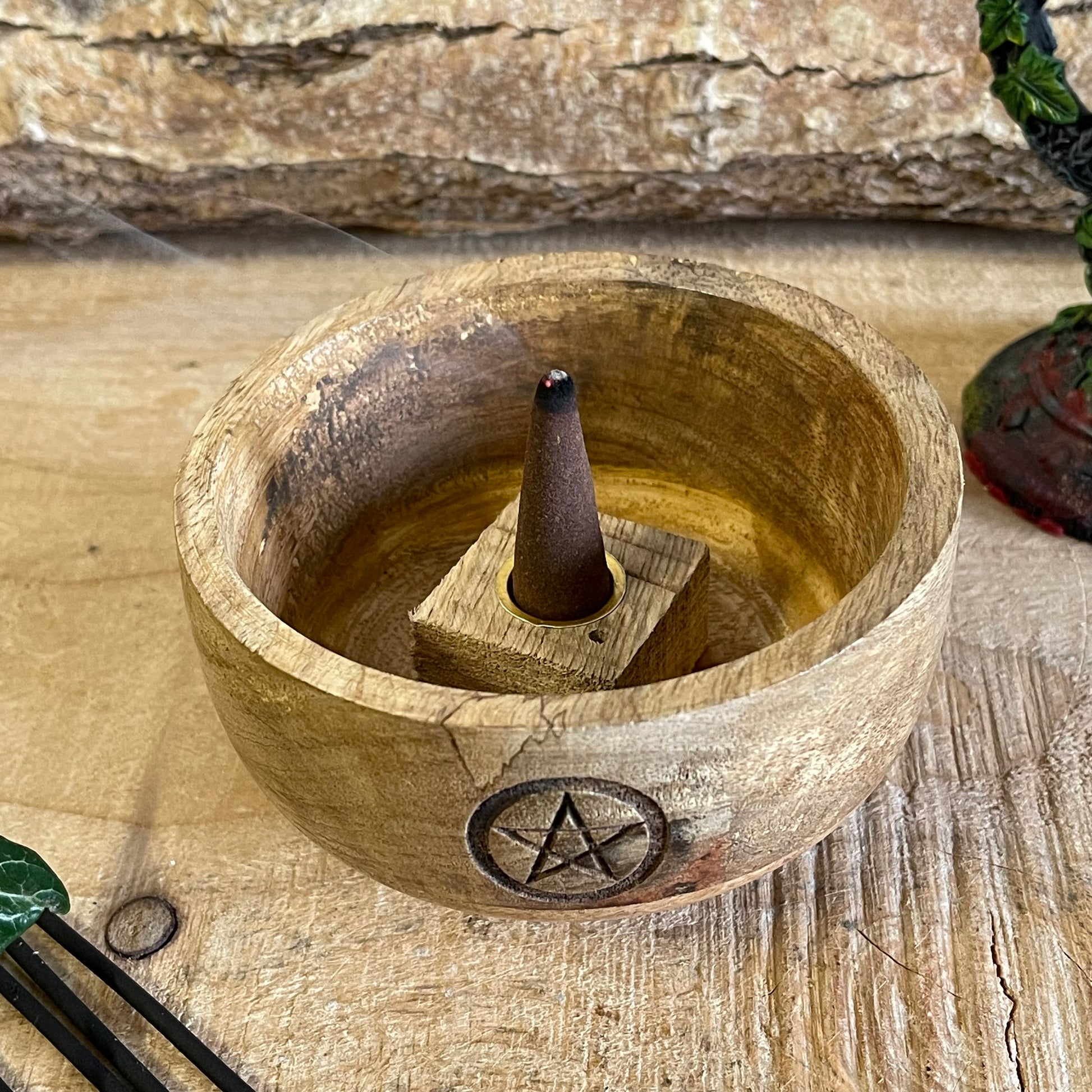 This incense holder is a compact, handcrafted wooden bowl with a rustic charm. Measuring 11 cm in diameter and 6 cm in height, it is designed to hold both incense sticks and cones. The highlight of this piece is the pentacle symbol, carefully etched onto the inside of the bowl, which adds a mystical, spiritual touch. The pentacle, often associated with protection and the elements, makes it ideal for meditation or ritualistic practices. The wood’s natural grain adds an earthy texture, enhancing its aesthetic