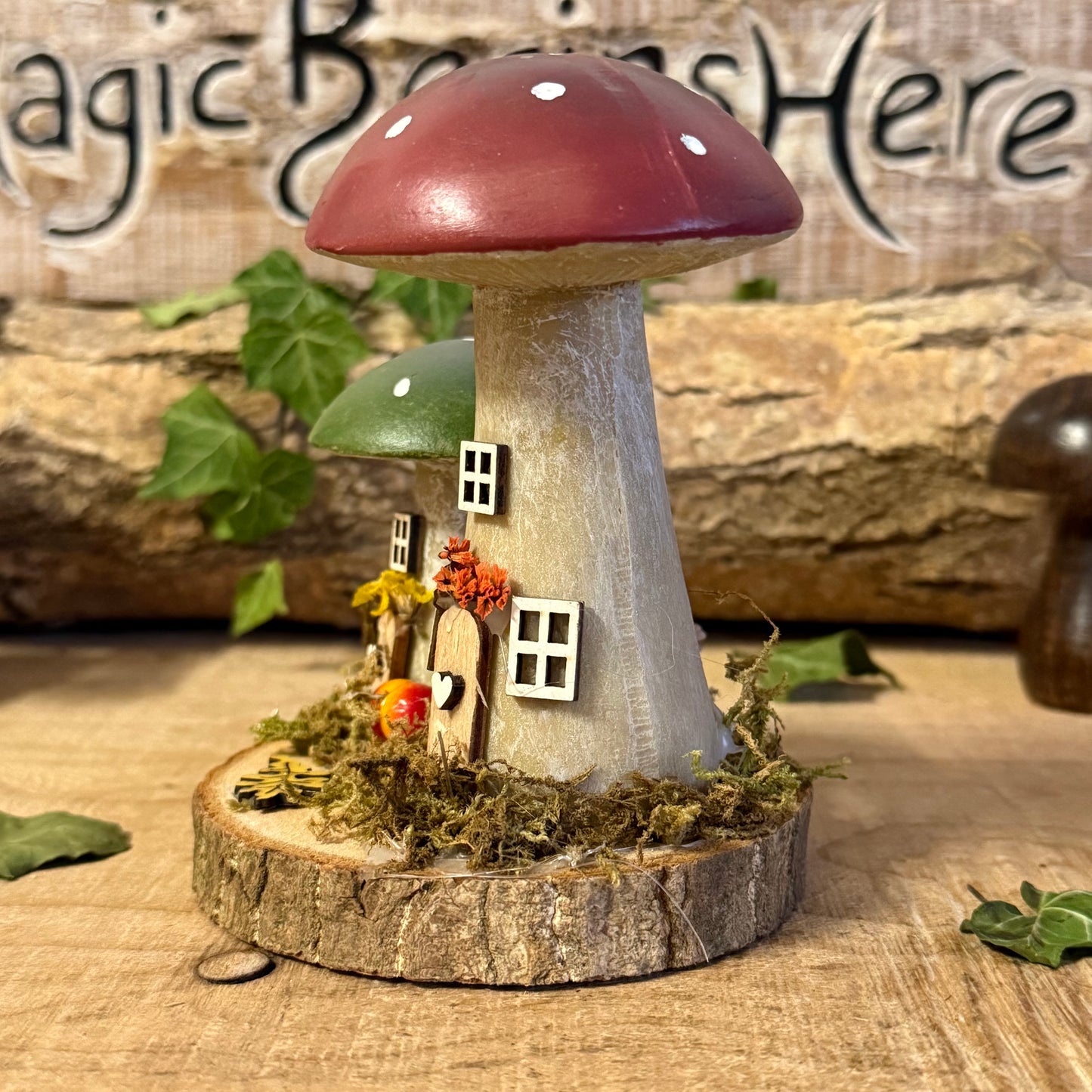 Wander into a whimsical woodland with our Folk Art Mushroom Two Cottages (Tall) — a delightful pair of hand painted fairy houses inspired by rustic village life and the charm of springtime meadows. Each tall mushroom cottage is adorned with bright folk art patterns, floral details, and earthy tones that bring a sense of storybook enchantment to your home.