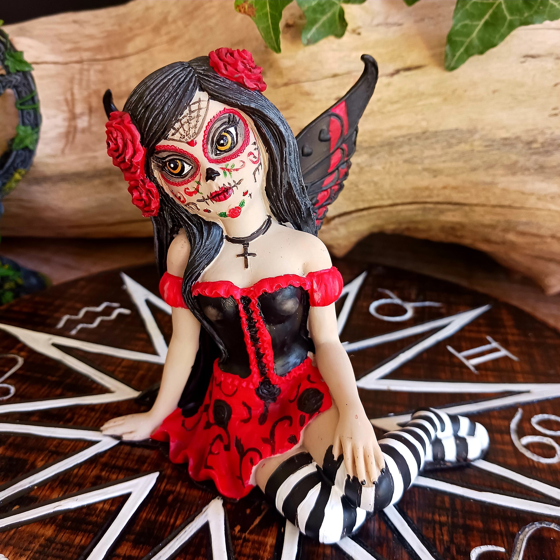 This stunning Fairy, Rosalia, was created by Fantasy brand Nemesis Now. She innocently sits with her striped legs extended to the side, wearing a black corseted dress that has a red skirt detailed with black roses.