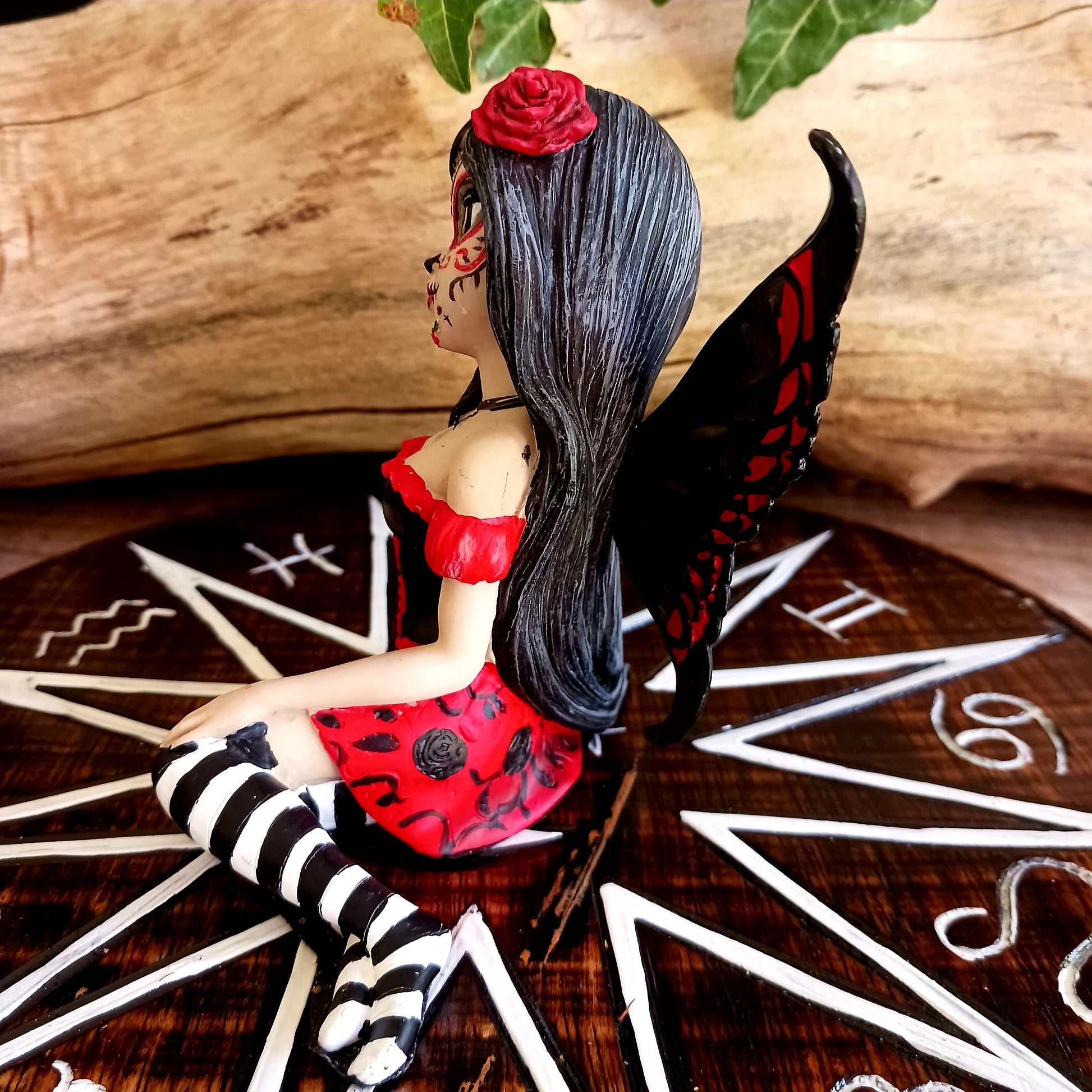 This stunning Fairy, Rosalia, was created by Fantasy brand Nemesis Now. She innocently sits with her striped legs extended to the side, wearing a black corseted dress that has a red skirt detailed with black roses.