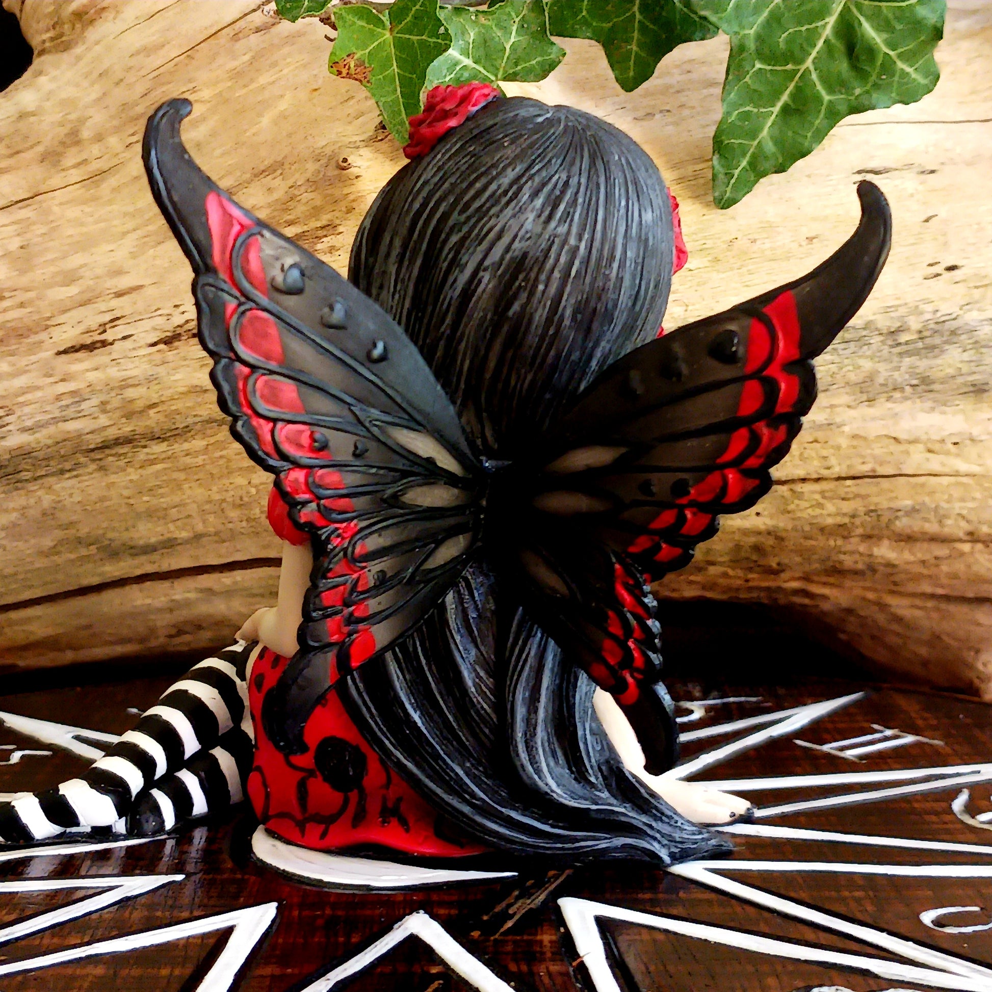 This stunning Fairy, Rosalia, was created by Fantasy brand Nemesis Now. She innocently sits with her striped legs extended to the side, wearing a black corseted dress that has a red skirt detailed with black roses.