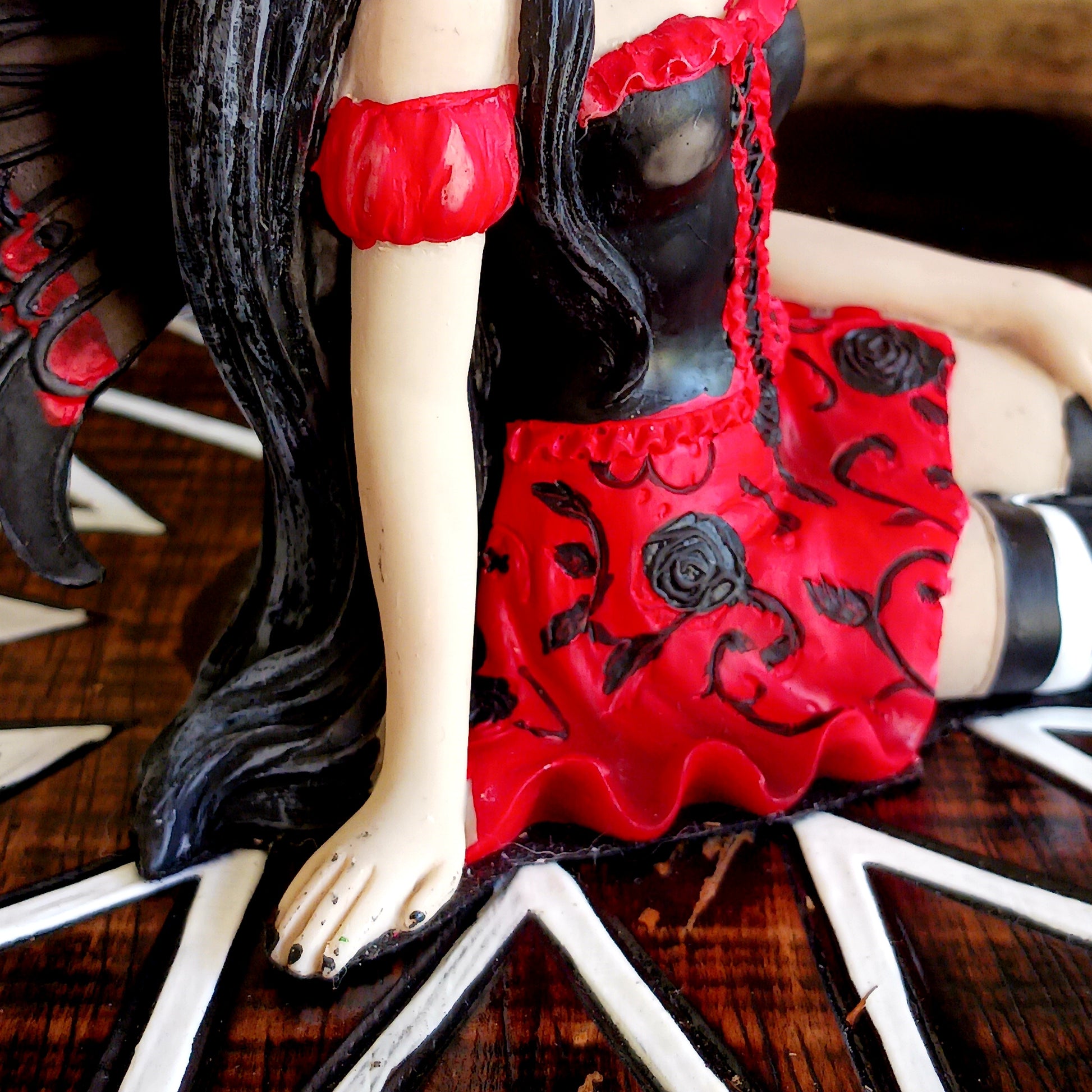 This stunning Fairy, Rosalia, was created by Fantasy brand Nemesis Now. She innocently sits with her striped legs extended to the side, wearing a black corseted dress that has a red skirt detailed with black roses.