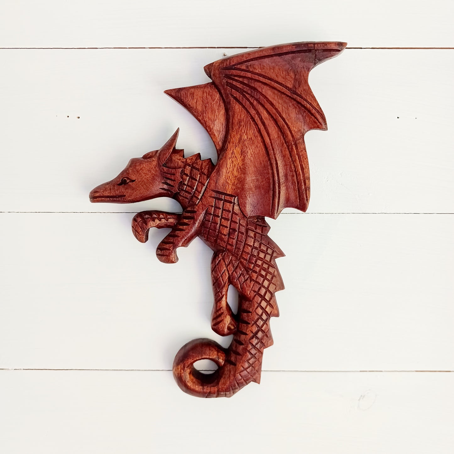 This intricately carved Dragon plaque sit flush against the wall or can be hooked onto pots or some other items in the home.&nbsp; These Dragons are hand carved with metal hook for hanging if you choose.  In early cultures, the dragons were often seen as mighty serpents and beasts that were either extremely benevolent or fearsome and difficult to kill. The beliefs of a region are often influenced by geographical location. Eastern cultures often saw dragons as a knowledgeable deity that had power over storms