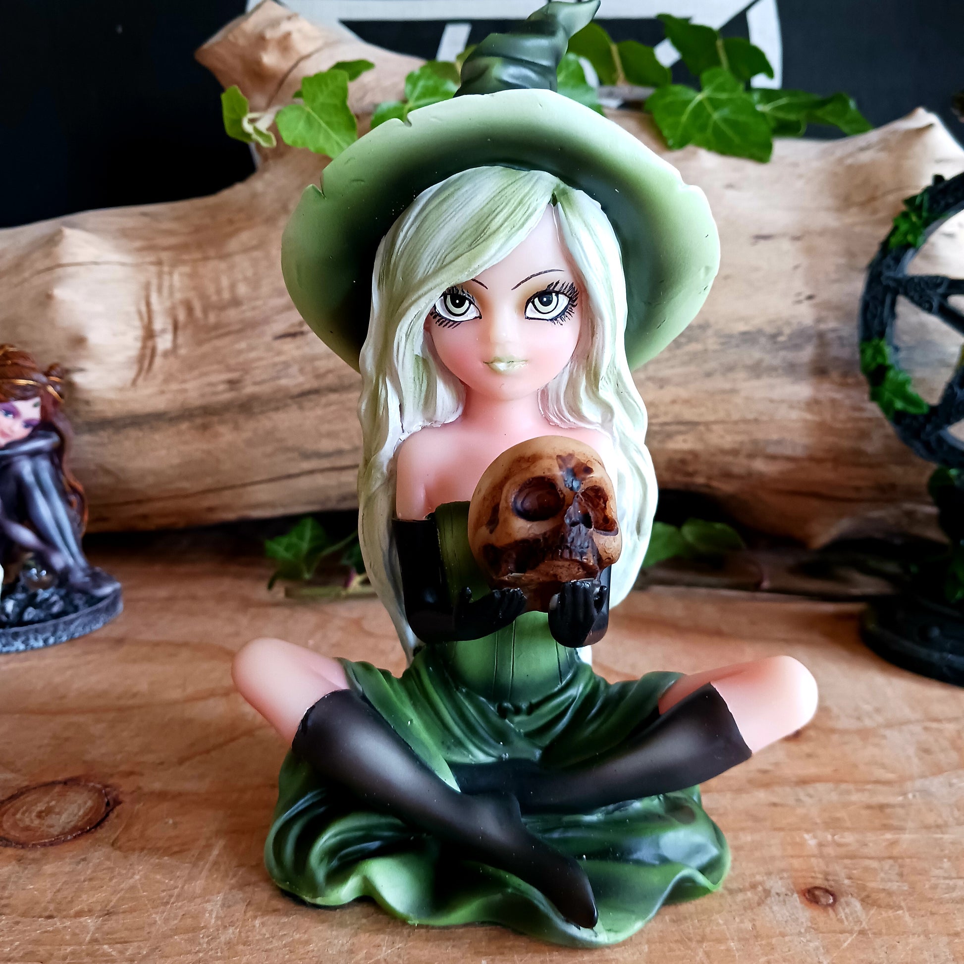 Wearing a matching green dress and pointy hat, Zelda sits crossed legged on the floor holding a human skull. Her stunning face is made up and is beautifully framed by her long blond hair, detailed with lime highlights.