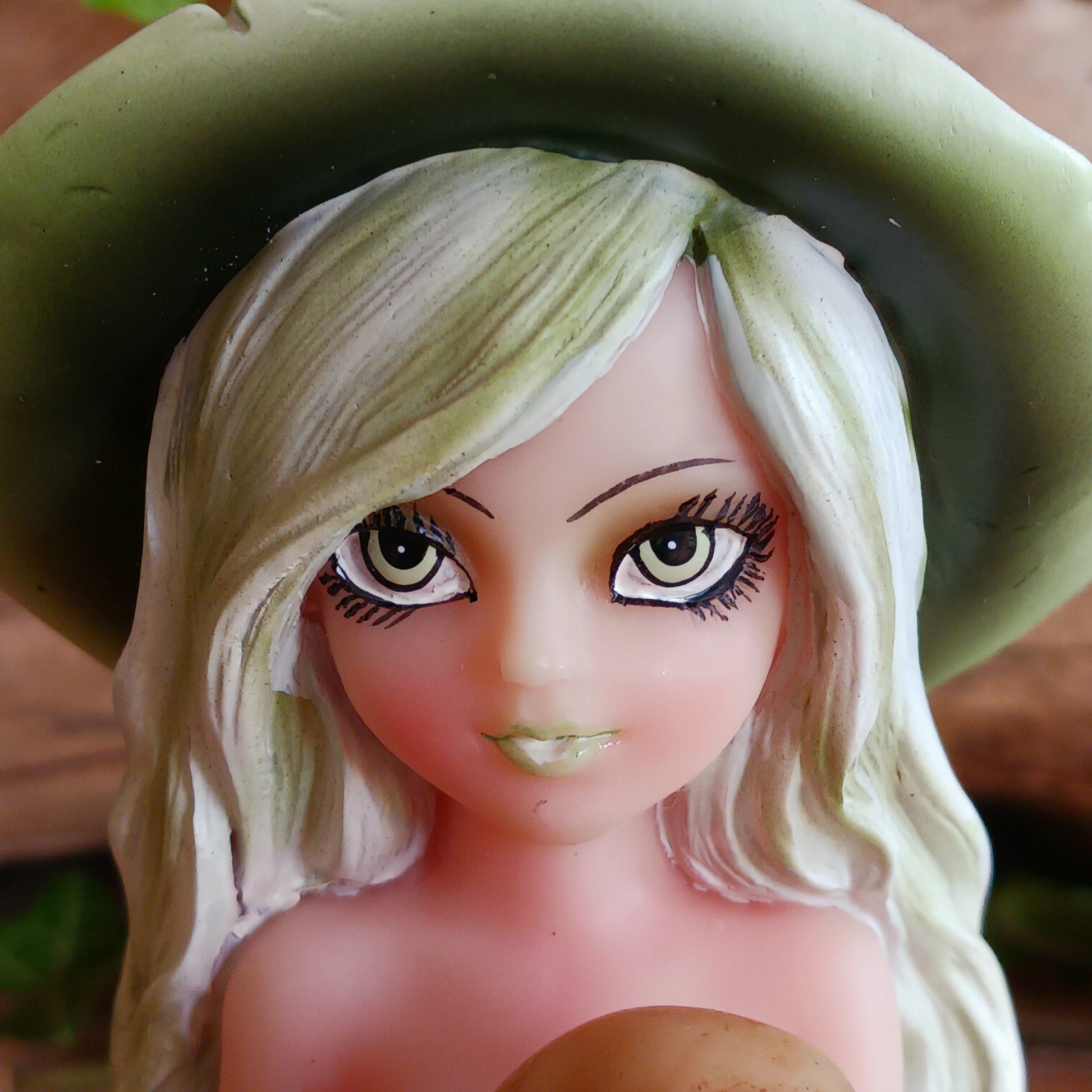 Wearing a matching green dress and pointy hat, Zelda sits crossed legged on the floor holding a human skull. Her stunning face is made up and is beautifully framed by her long blond hair, detailed with lime highlights.