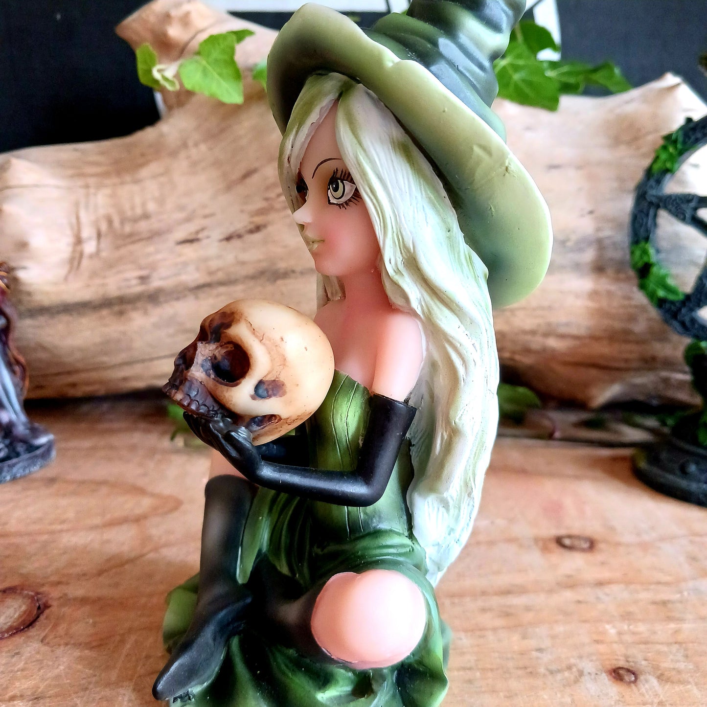 Wearing a matching green dress and pointy hat, Zelda sits crossed legged on the floor holding a human skull. Her stunning face is made up and is beautifully framed by her long blond hair, detailed with lime highlights.