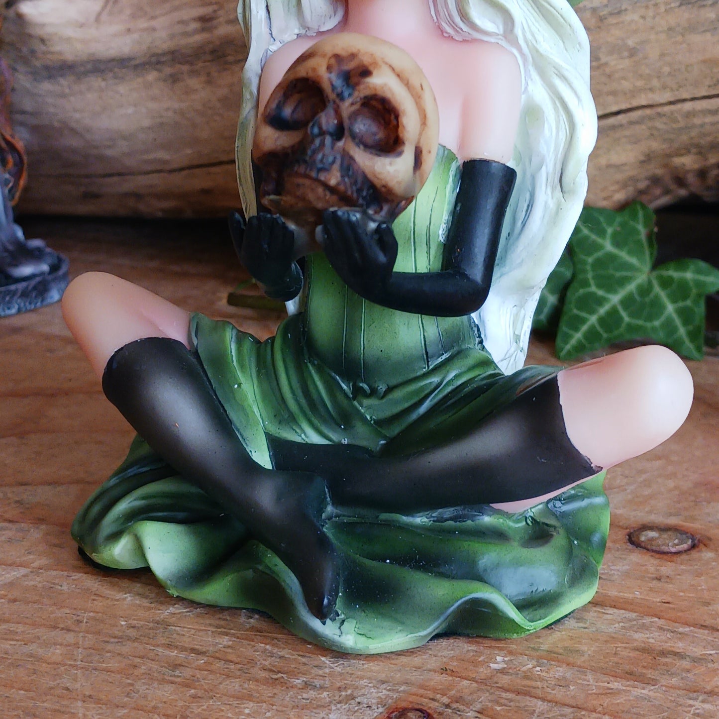 Wearing a matching green dress and pointy hat, Zelda sits crossed legged on the floor holding a human skull. Her stunning face is made up and is beautifully framed by her long blond hair, detailed with lime highlights.