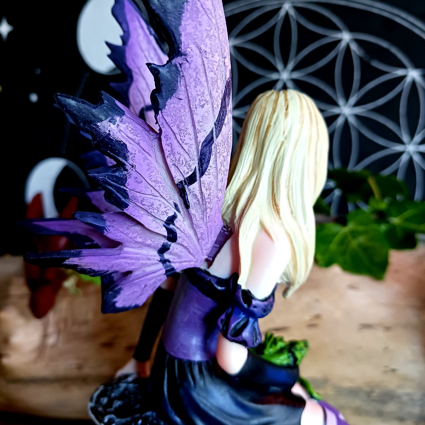 Sitting on a natural pillar of rock, this purple-winged Fairy looks to the side, blonde hair ending past her shoulders. On her shoulder, a purple Dragon hatchling looks around at the world cautiously, their green sibling curling defensively on the Fairy's lap. Around her feet, more Dragons hatch from bone-coloured eggs, taking their first look at the world. On the Fairy's forehead, a mystical symbol is marked in purple.