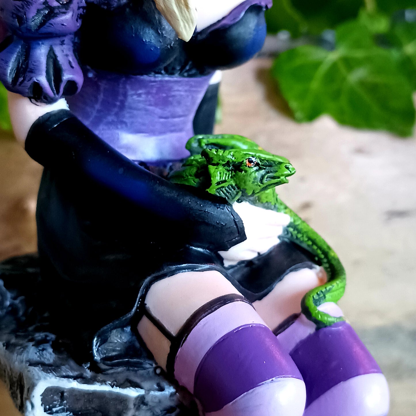 Sitting on a natural pillar of rock, this purple-winged Fairy looks to the side, blonde hair ending past her shoulders. On her shoulder, a purple Dragon hatchling looks around at the world cautiously, their green sibling curling defensively on the Fairy's lap. Around her feet, more Dragons hatch from bone-coloured eggs, taking their first look at the world. On the Fairy's forehead, a mystical symbol is marked in purple.