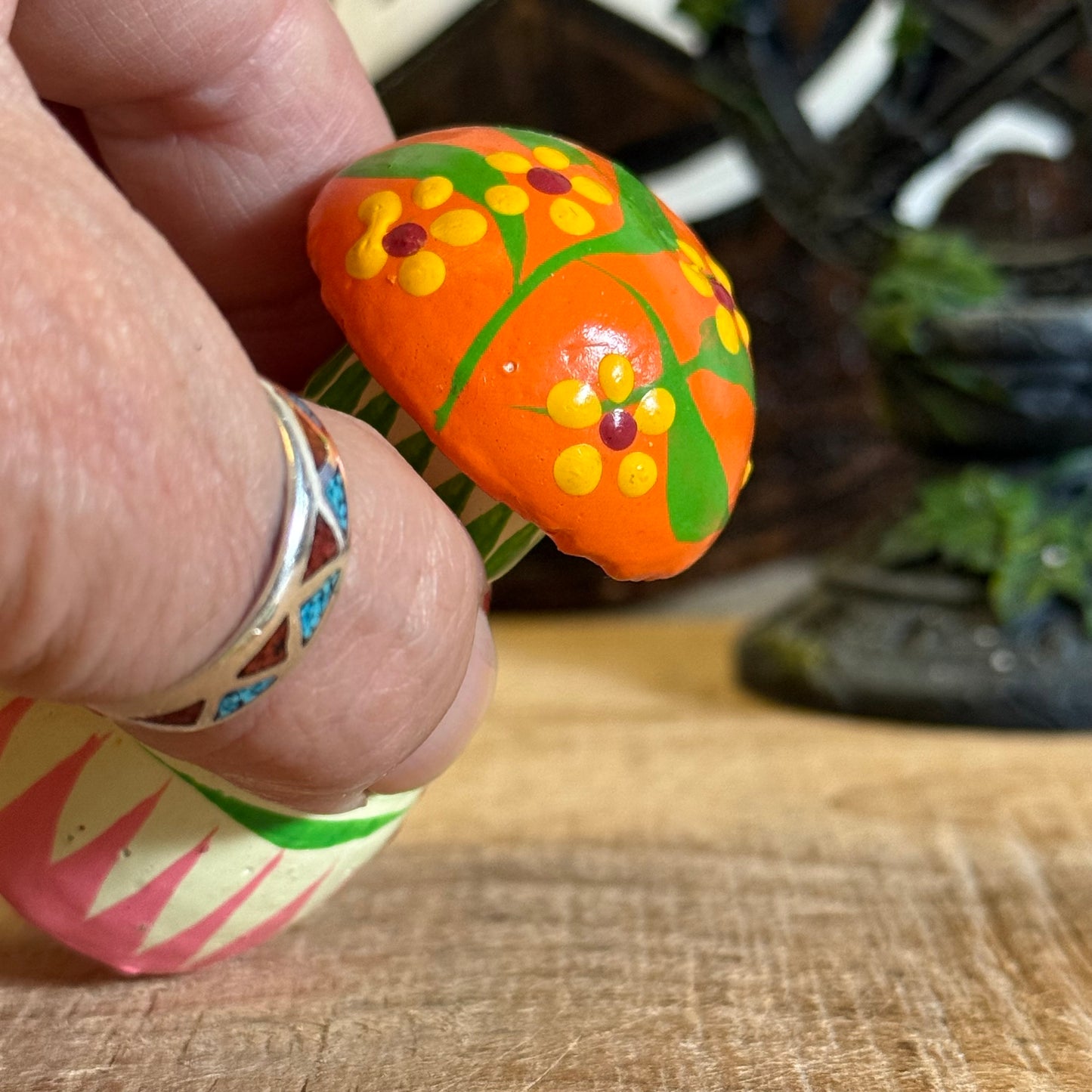 Hand holding a colorful painted stone with floral design on a wooden surface