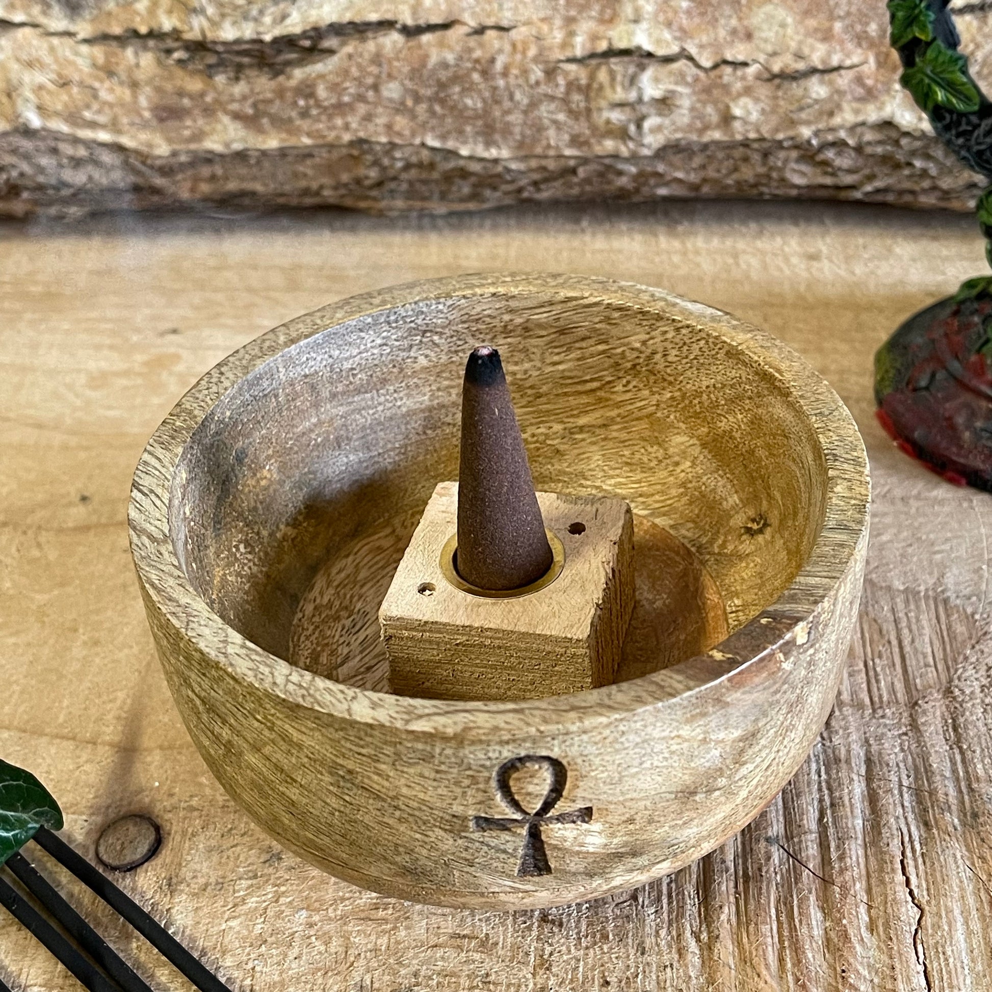 This incense holder is a compact, handcrafted wooden bowl, measuring approximately 11 cm in diameter and 6 cm in height. It features an engraving of the Ankh, also known as the Key of Life, a symbol associated with life and protection in ancient Egyptian culture. The Ankh etching adds a mystical and meaningful touch to the piece, blending spirituality with functionality.

The design accommodates both incense sticks and incense cones. The bowl is likely shaped to safely catch ash, with designated holders or 