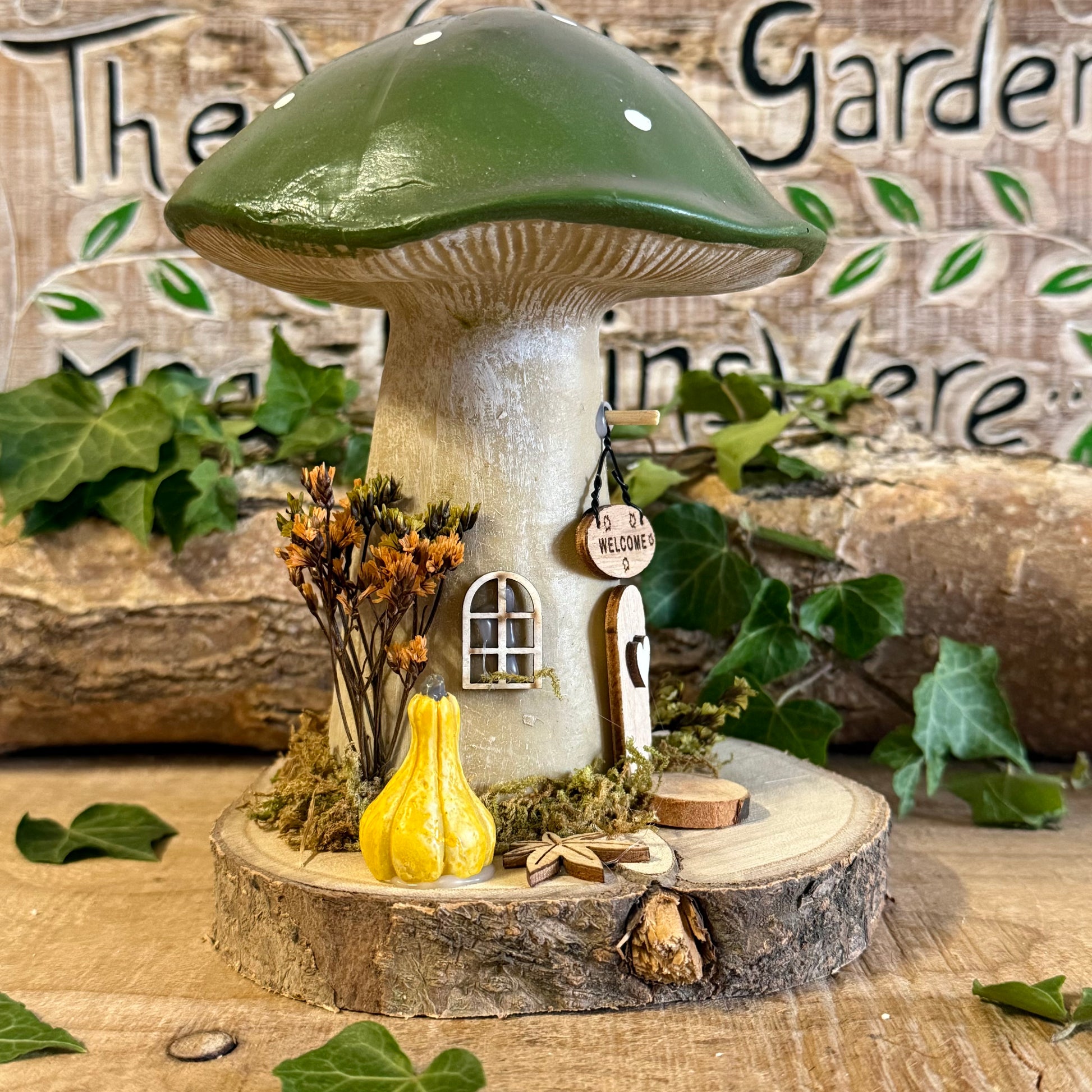 Welcome all who wander with this charming Folk Art Mushroom Cottage with Welcome Sign (Large) — a beautifully hand painted fairy house inspired by woodland folklore and cosy forest living. Its bright toadstool roof, delicate floral detailing, and rustic textures create the feeling of a tiny cottage nestled beneath ancient trees.