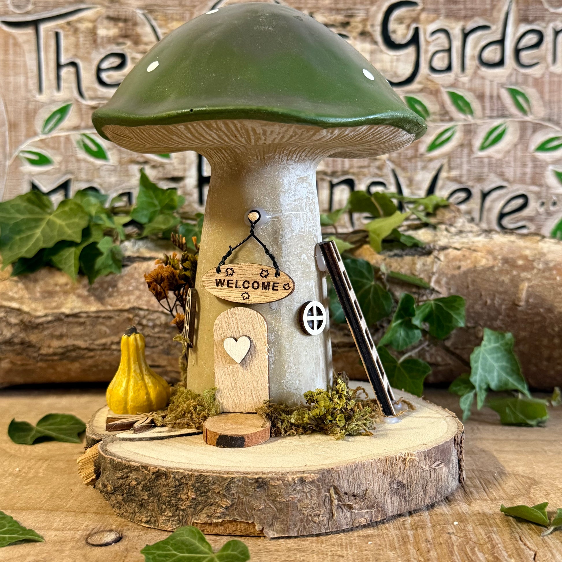 Welcome all who wander with this charming Folk Art Mushroom Cottage with Welcome Sign (Large) — a beautifully hand painted fairy house inspired by woodland folklore and cosy forest living. Its bright toadstool roof, delicate floral detailing, and rustic textures create the feeling of a tiny cottage nestled beneath ancient trees.