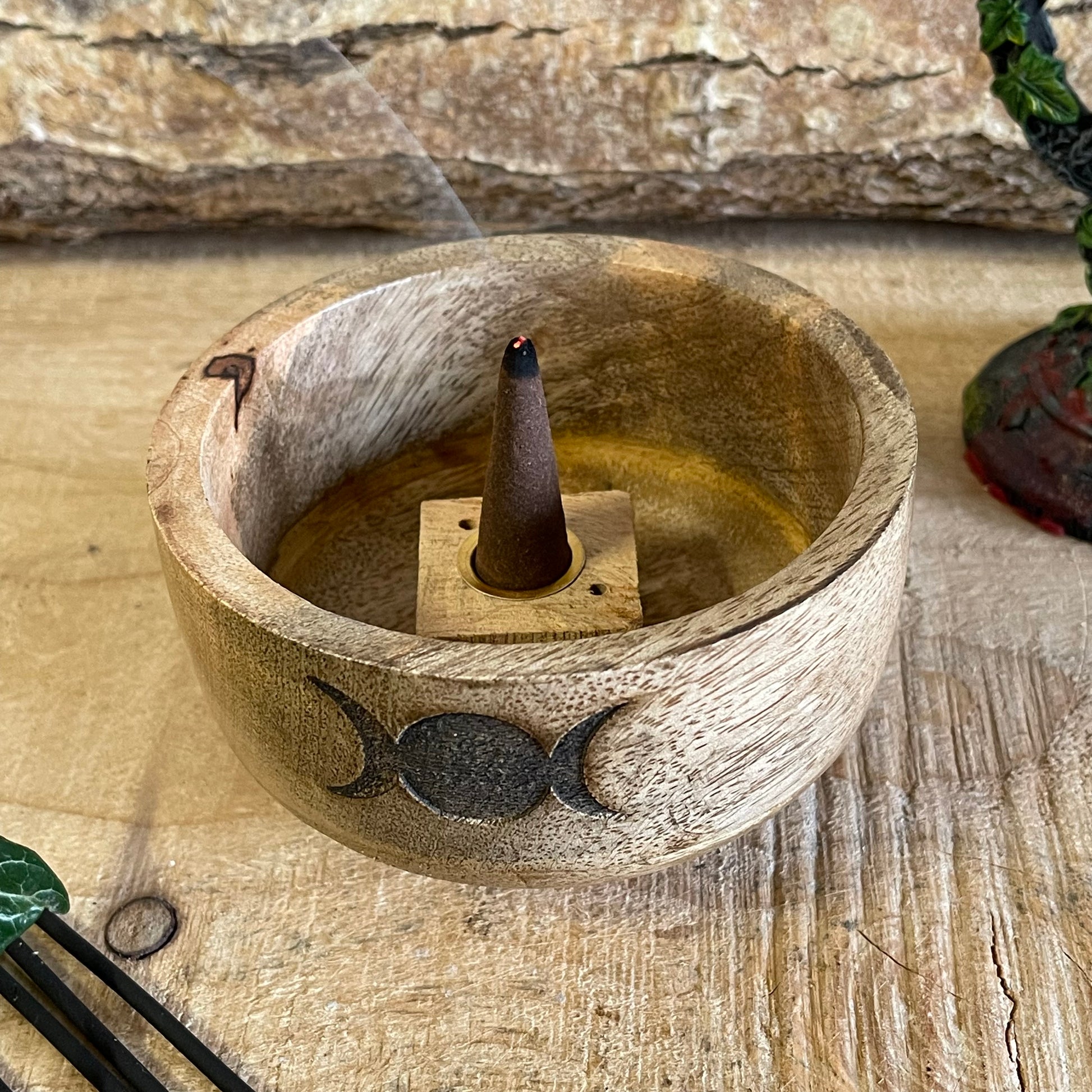 This incense holder is a compact and beautifully crafted wooden bowl measuring 11 cm in diameter and 6 cm in height. Its design features the Triple Moon symbol, representing the phases of the moon: waxing, full, and waning. This symbol is etched into the wood, giving it a subtle yet mystical appeal, which is often associated with spiritual growth, intuition, and the goddess in many traditions.