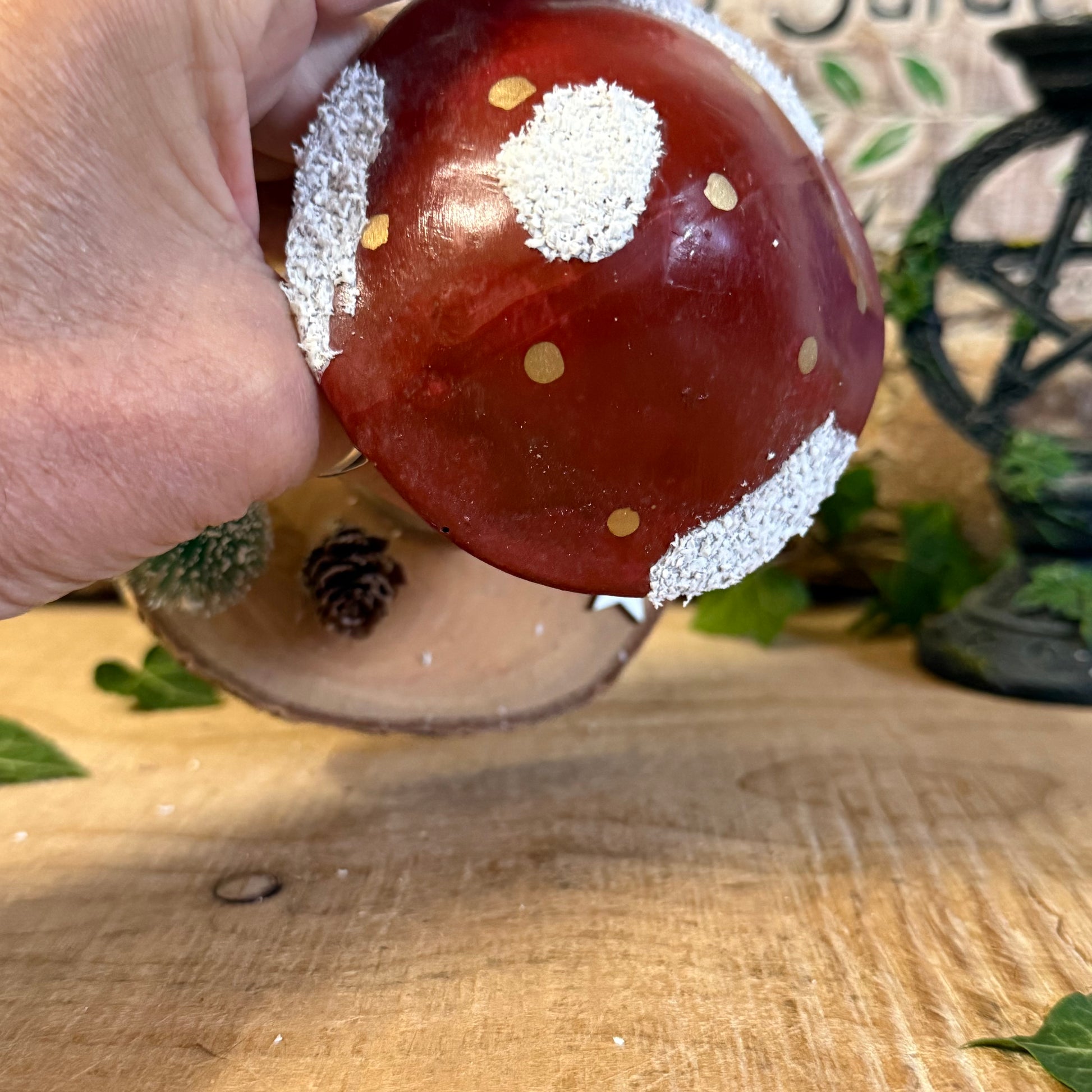 Decorative mushroom ornament with white spots held by a hand on a wooden surface.