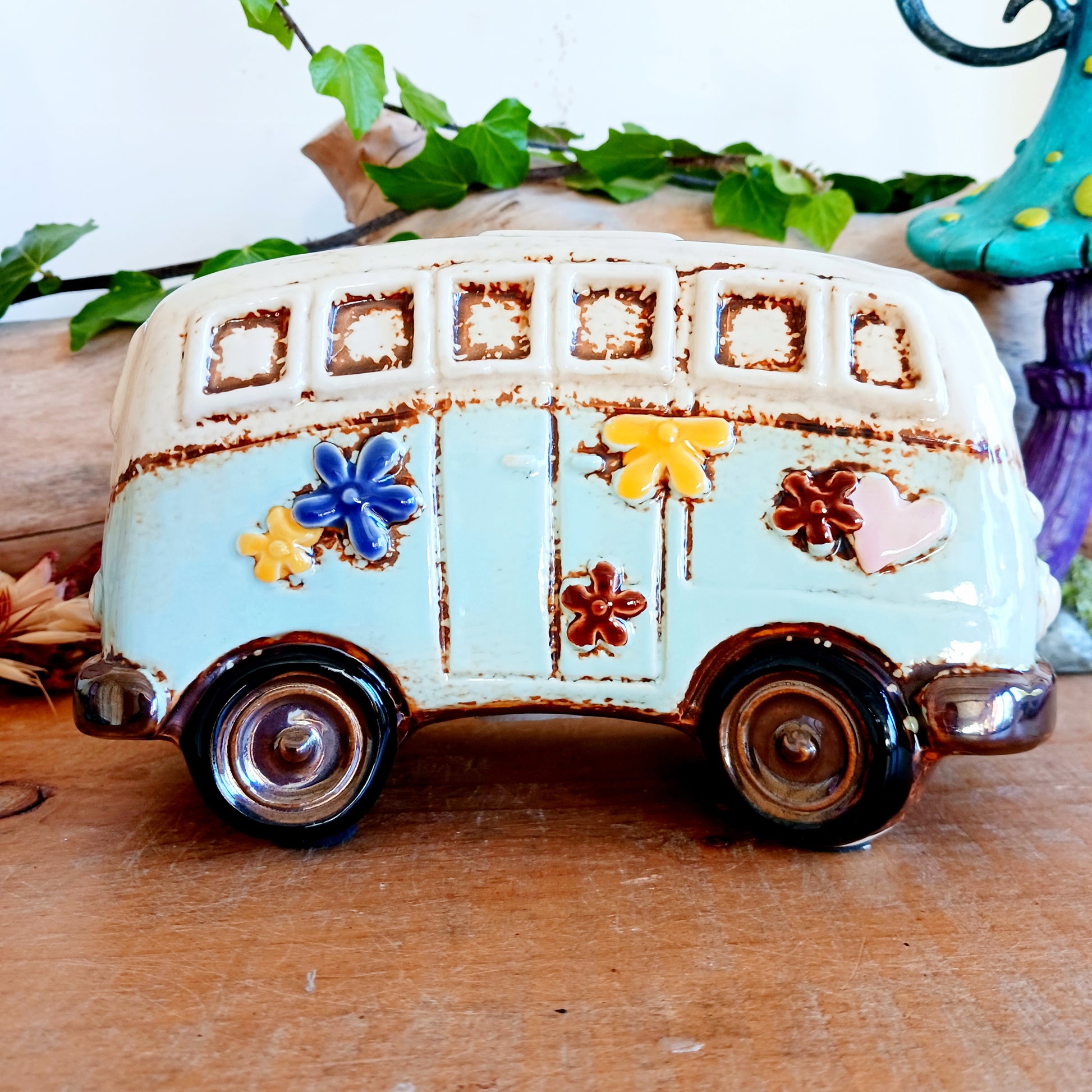 From the enchanted lanes of Village Pottery comes this Aqua VW Campervan Money Box, a charming ceramic treasure crafted for dreamers and wanderers alike. Measuring 11 x 18.5 x 10cm, this delightful piece captures the spirit of adventure with its soft aqua glaze, vintage VW Campervan design, and hand-painted detailing that feels kissed by fairy dust.