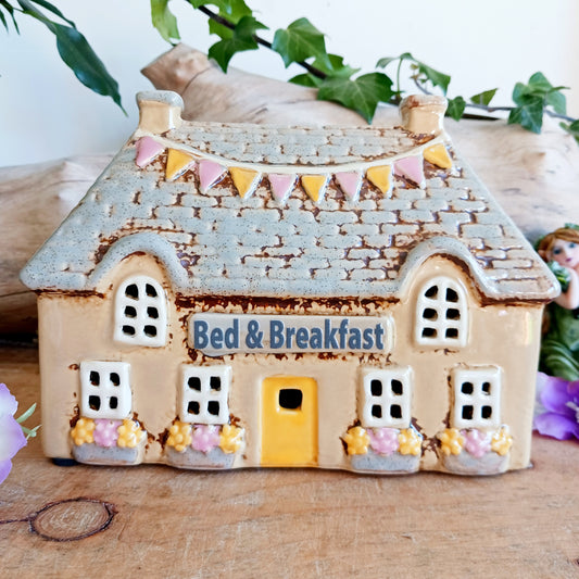 A welcoming glow awaits within this Village Pottery Bed & Breakfast Tealight House, where candlelight flickers through tiny windows like a hearth lit for wandering souls. Crafted from ceramic, this charming inn captures the spirit of an enchanted village, inviting warmth, stillness, and quiet magic into your space.