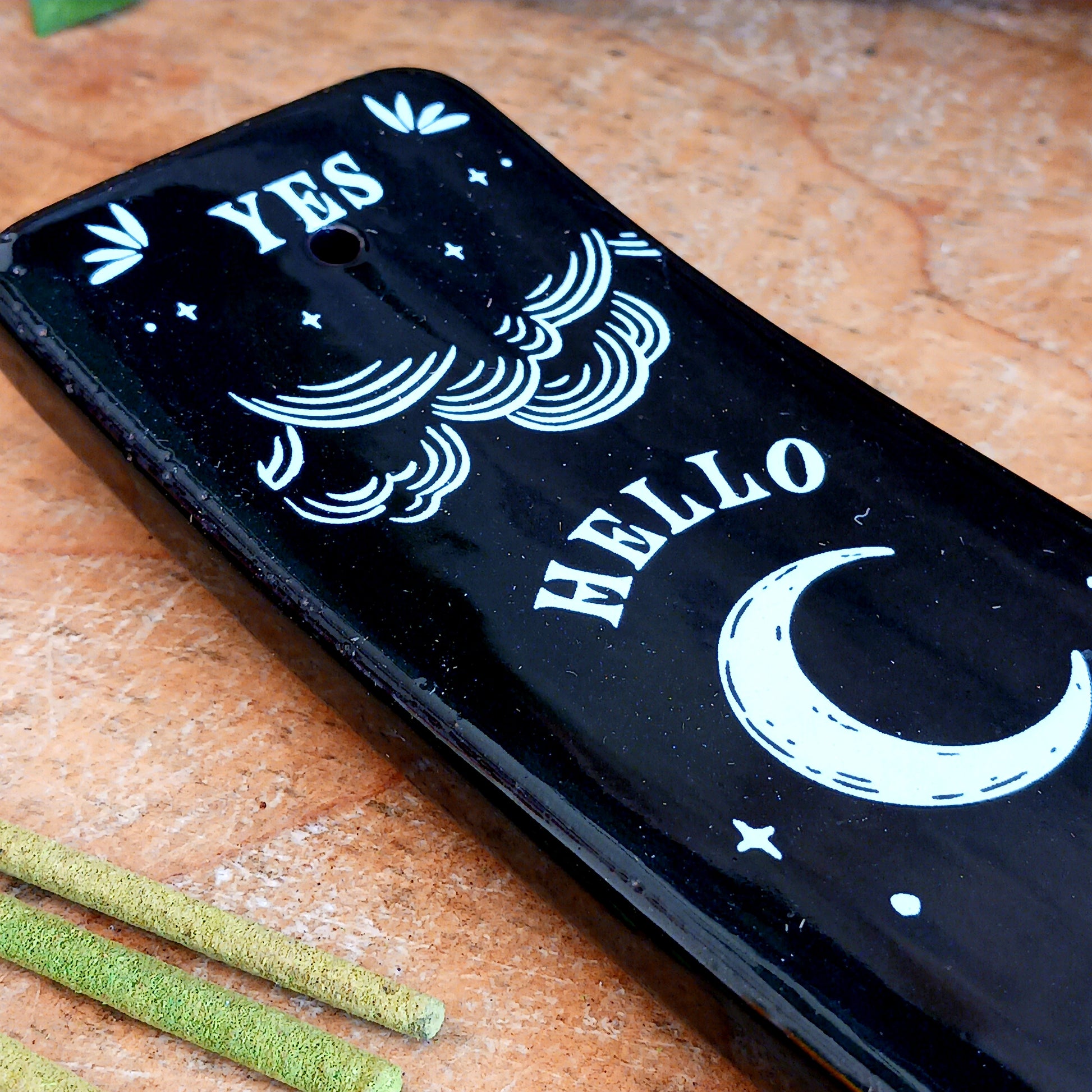 Add a touch of mystical gothic style to your incense rituals with this striking black incense ash catcher, inspired by traditional talking boards. Featuring a decorative planchette-style design surrounded by stars, moons and an all-seeing eye, it creates an atmospheric setting for burning your favourite incense sticks.