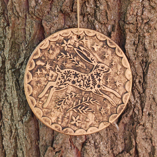 Add a touch of seasonal magic to your home or garden with this enchanting Winter Solstice Hare Hanging Plaque. Crafted from terracotta and finished with an attractive brushed bronze effect, the plaque features an elegant leaping hare surrounded by intricate botanical detailing inspired by the beauty of the natural world.