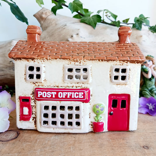 Whispers travel by candlelight from this Village Pottery Post Office tealight house, where tiny windows glow like messages carried between realms. Crafted from ceramic and measuring 12x15x7cm, this enchanting piece brings warmth and quiet magic to your sacred space.