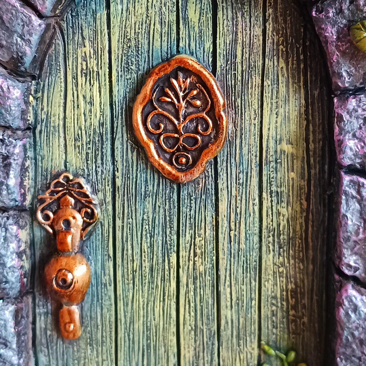 Step into a world of wonder with the Fae’s Forest Welcome fairy door. This beautifully crafted piece features a forest-green wooden-textured door framed by a detailed stone arch, adorned with twisting vines and bright red and yellow flowers.
