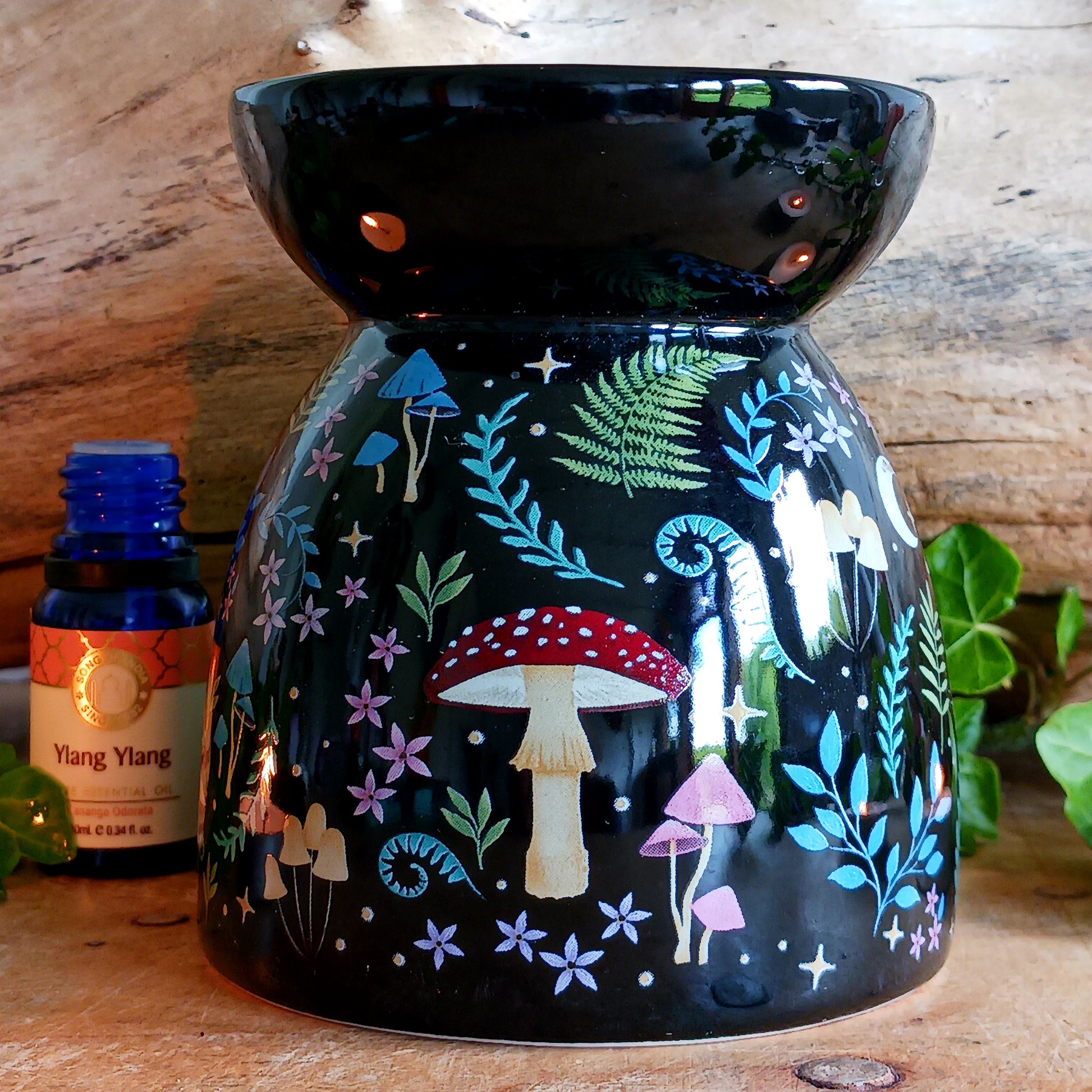 Transform your space into a magical woodland retreat with this beautifully designed dark forest oil burner. Featuring a rich black finish adorned with vibrant illustrations of flora and fauna, this enchanting piece comes to life when lit, casting a warm, ambient glow reminiscent of moonlit nights beneath the stars.