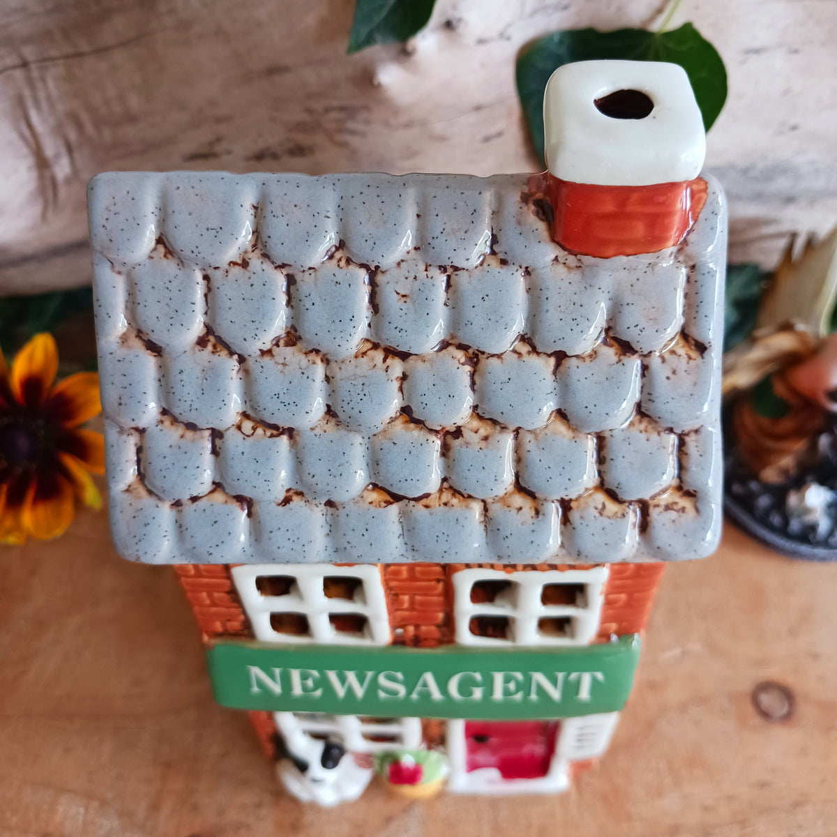 Bring a touch of village charm to your home with the Village Pottery Newsagent Tealight Holder. Beautifully designed as a traditional little village newsagent, this charming ceramic tealight holder features a warm red-brick façade, textured cream tiled roof and cheerful bright red front door.