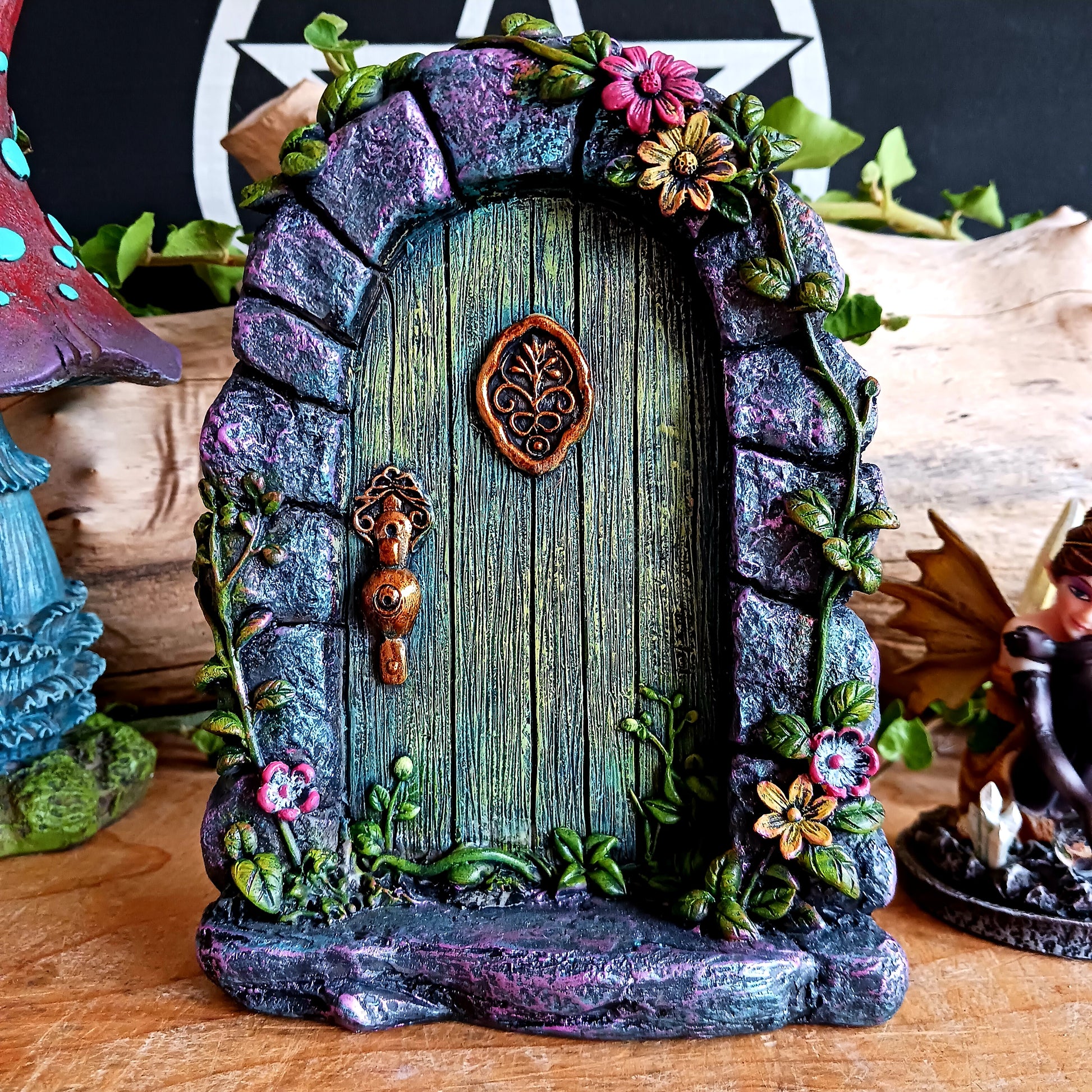 Step into a world of wonder with the Fae’s Forest Welcome fairy door. This beautifully crafted piece features a forest-green wooden-textured door framed by a detailed stone arch, adorned with twisting vines and bright red and yellow flowers.