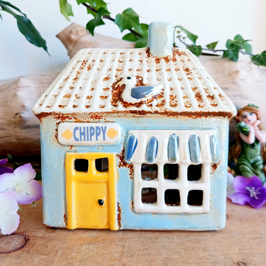 A warm, golden glow spills from the windows of this Village Pottery Chippy, where the spirit of a bustling village meets quiet enchantment. Crafted from ceramic, this Shudehill tealight house captures a familiar yet mystical charm, as candlelight flickers like stories shared after dusk.
