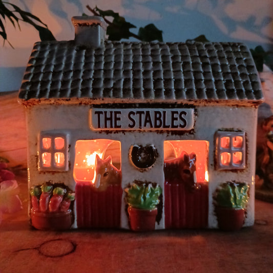 Nestled at the edge of a quiet enchanted village, The Stables tealight house by Village Pottery glows with a soft, grounding warmth. Crafted from ceramic and measuring 17x8x8cm, this rustic stable invites candlelight to flicker through its windows like a lantern for wandering spirits and kindred souls.
