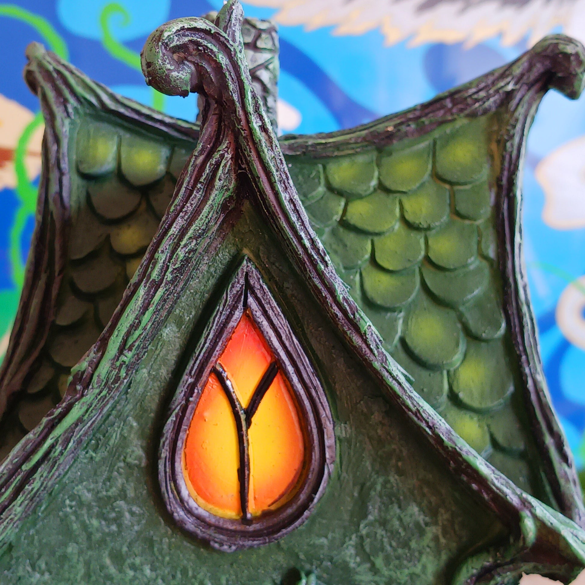 Step into a magical, enchanted forest with this beautiful gothic-style fairy cottage. Designed with a pointed roof adorned in dark green, scale-like shingles, this stunning piece glows warmly with LED lights shining through medieval-style windows. Sculpted vines and twisting tree roots climb the sides, while curled roof details add an intricate, whimsical finish.