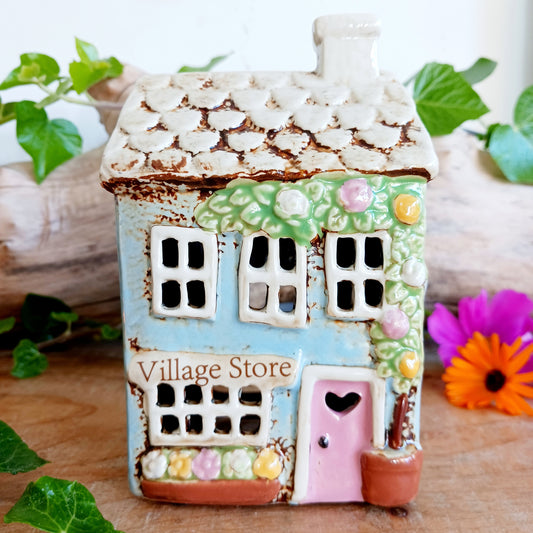 Welcome a touch of storybook charm into your home with the Village Pottery Village Stores Tealight Holder, a handcrafted ceramic delight glowing with the warmth of simpler times. Measuring 15.5 x 9.5 x 8 cm, this quaint miniature shop captures the heart of an old-fashioned village, complete with detailed windows, rustic roof tiles, and painted signage that evokes cosy nostalgia.