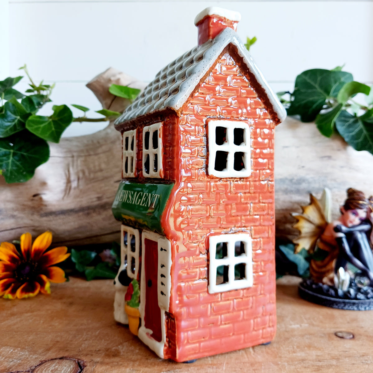 Bring a touch of village charm to your home with the Village Pottery Newsagent Tealight Holder. Beautifully designed as a traditional little village newsagent, this charming ceramic tealight holder features a warm red-brick façade, textured cream tiled roof and cheerful bright red front door.