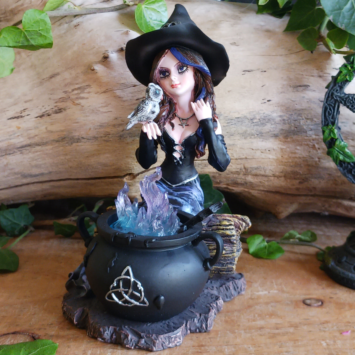 Meet Alvina, a captivating hand-painted witch figurine seated peacefully on a rustic log with her enchanting owl companion. Dressed in a flowing blue gown with long brown hair, Alvina has a mysterious yet charming presence that will appeal to lovers of witches, fantasy and magical décor.