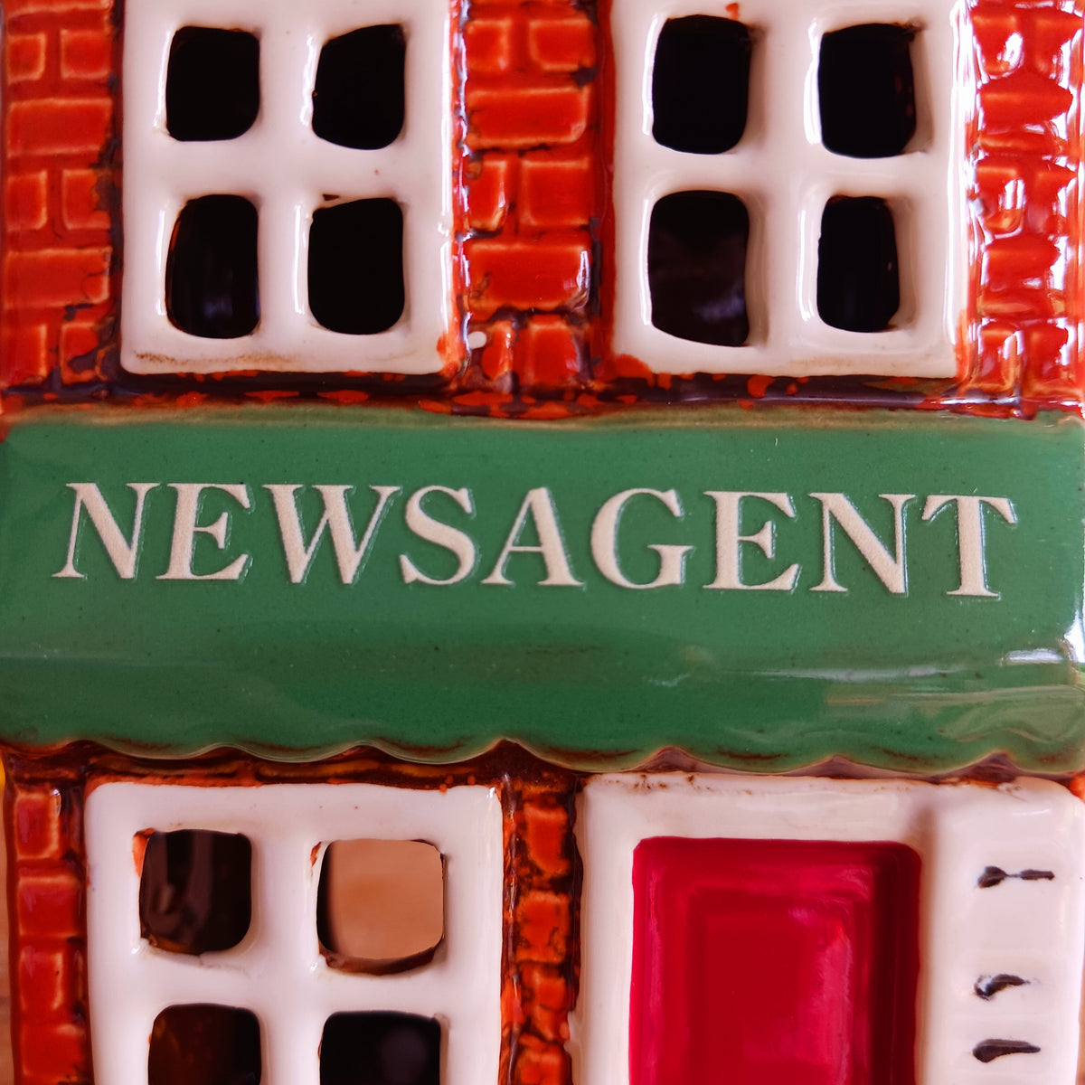 Bring a touch of village charm to your home with the Village Pottery Newsagent Tealight Holder. Beautifully designed as a traditional little village newsagent, this charming ceramic tealight holder features a warm red-brick façade, textured cream tiled roof and cheerful bright red front door.