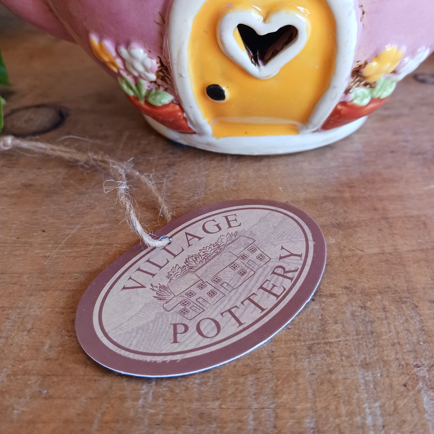 Add a sprinkle of charm to your home with this adorable Village Pottery ceramic tealight holder, beautifully designed as a whimsical pink teapot transformed into a cosy village tea shop. Featuring cottage-style windows, colourful bunting, pretty floral details and a welcoming heart-shaped doorway, this delightful decorative piece brings a touch of storybook magic to any room.
