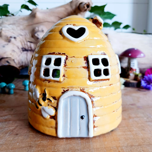 Bring a buzz of warmth and charm to your home with this Yellow Mini Beehive House Tealight Holder from Village Pottery. Expertly handcrafted and standing at 11.5cm tall, this delightful ceramic piece captures the rustic whimsy of a classic beehive. Its vibrant yellow glaze and tiny cut-out windows allow the soft glow of a tealight to flicker gently through, creating a cosy, inviting ambiance. Whether you're decorating your living room, bedroom, or outdoor space, this charming tealight holder adds a cheerful
