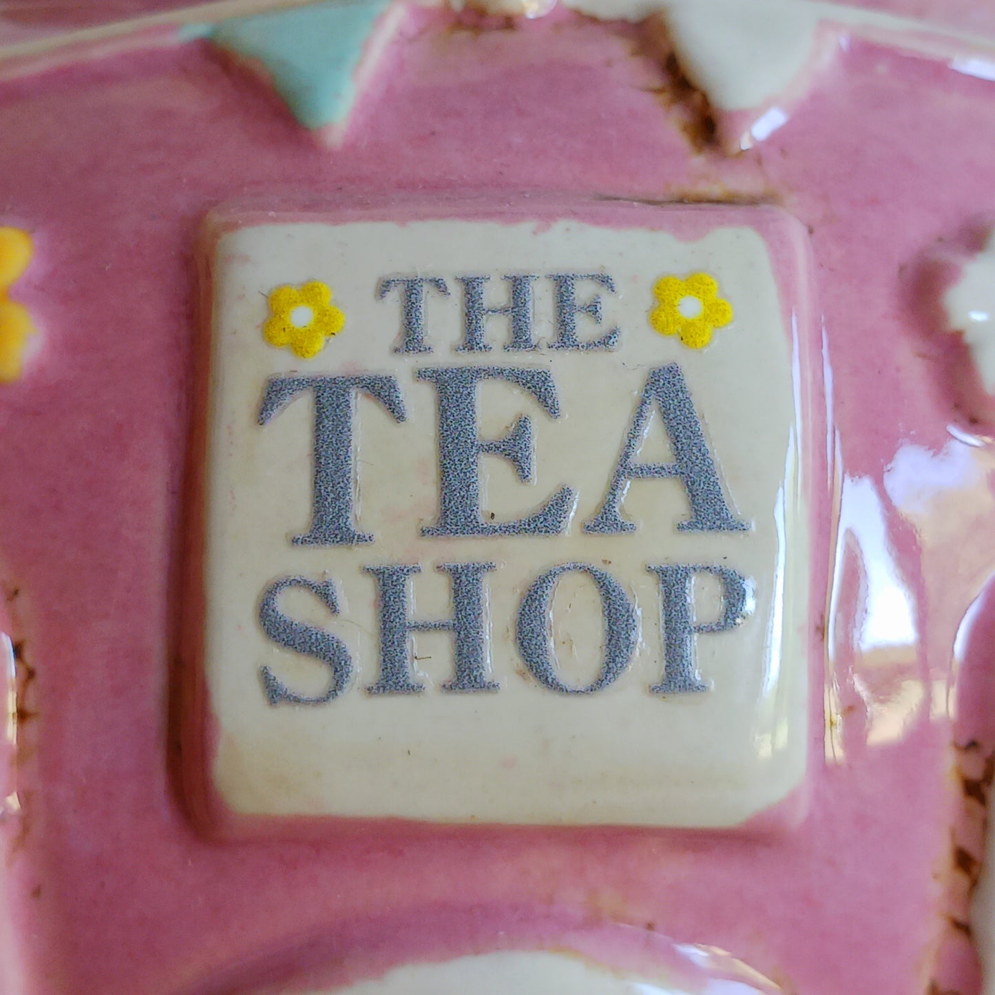 Add a sprinkle of charm to your home with this adorable Village Pottery ceramic tealight holder, beautifully designed as a whimsical pink teapot transformed into a cosy village tea shop. Featuring cottage-style windows, colourful bunting, pretty floral details and a welcoming heart-shaped doorway, this delightful decorative piece brings a touch of storybook magic to any room.