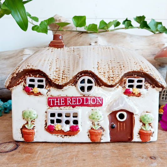 Illuminate your home with the charming Red Lion Pub Tealight Holder from the Village Pottery Collection. Crafted from quality ceramic, this delightful tealight holder adds warmth and character to any space. Perfect for creating your own enchanting village scene, it’s both a functional tealight holder and a decorative ornament.