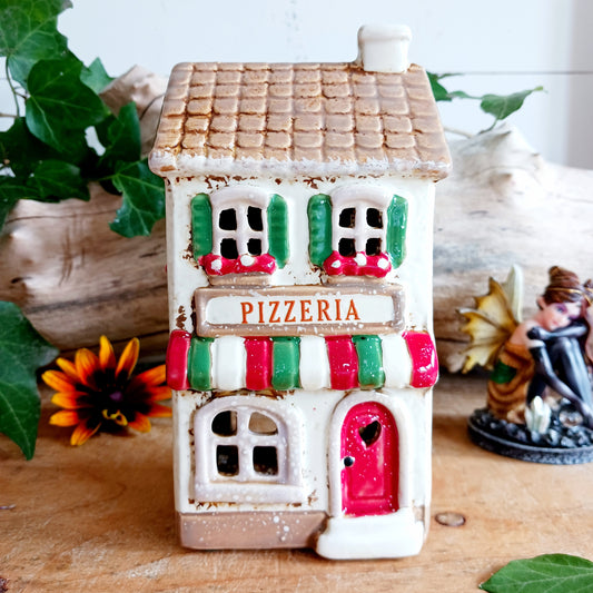 Bring a little taste of Italy into your home with this charming Village Pottery Pizzeria Tealight Holder. Designed as a delightful two-storey Italian village building, this cream pottery house features a brown tiled roof, chimney, green shutters, red flower boxes and colourful red and green striped awnings.