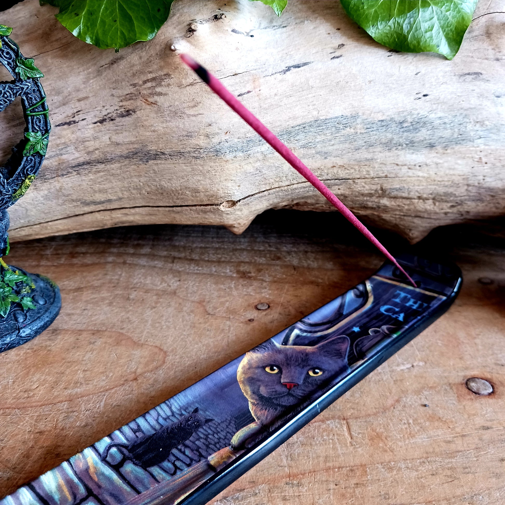Bring a touch of magic into your home with the enchanting Rusty Cauldron Incense Burner by renowned fantasy artist Lisa Parker. Featuring her iconic artwork, this beautifully crafted piece captures a mystical feline perched atop a barrel outside the legendary Rusty Cauldron, while another curious cat watches the magical high street unfold behind.