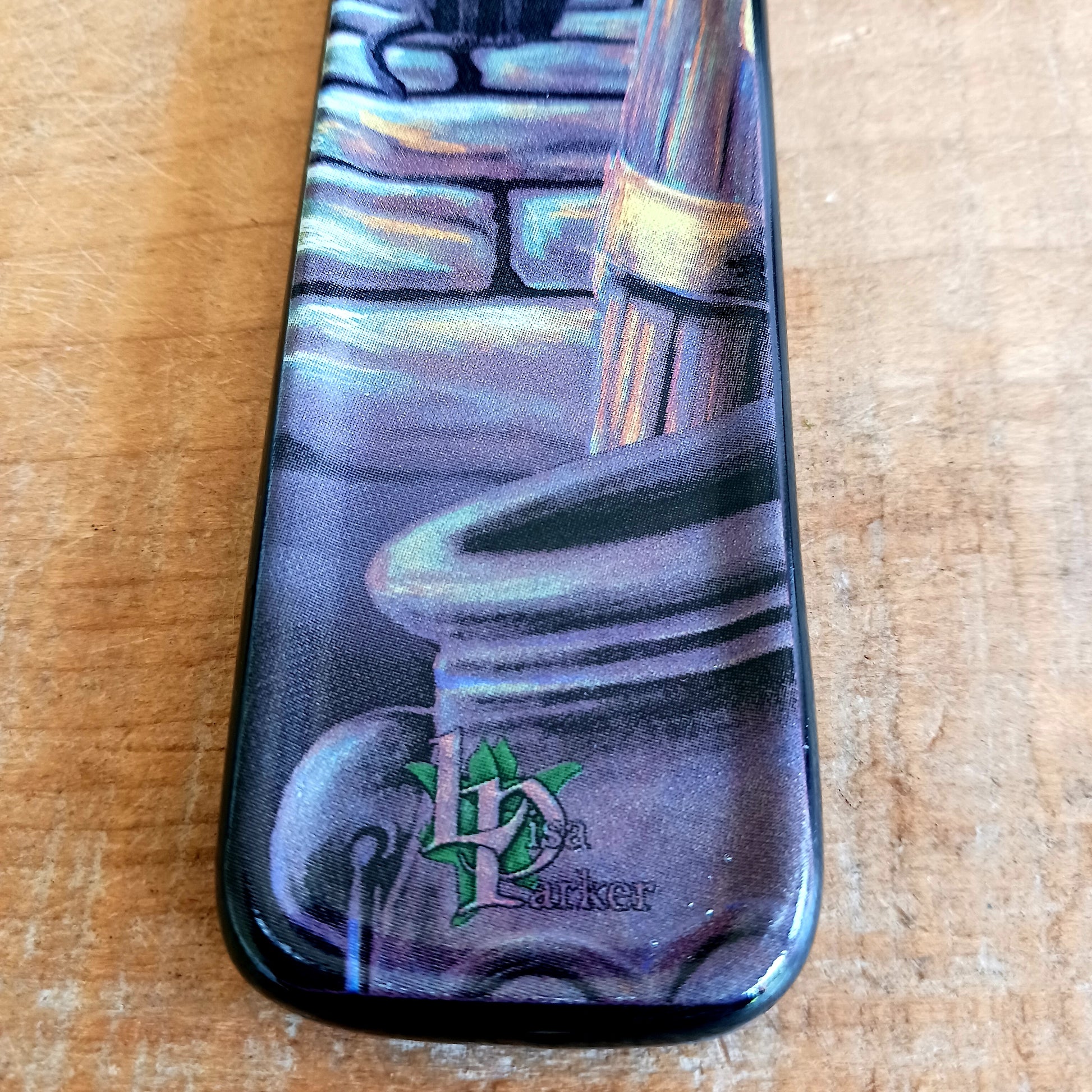 Bring a touch of magic into your home with the enchanting Rusty Cauldron Incense Burner by renowned fantasy artist Lisa Parker. Featuring her iconic artwork, this beautifully crafted piece captures a mystical feline perched atop a barrel outside the legendary Rusty Cauldron, while another curious cat watches the magical high street unfold behind.