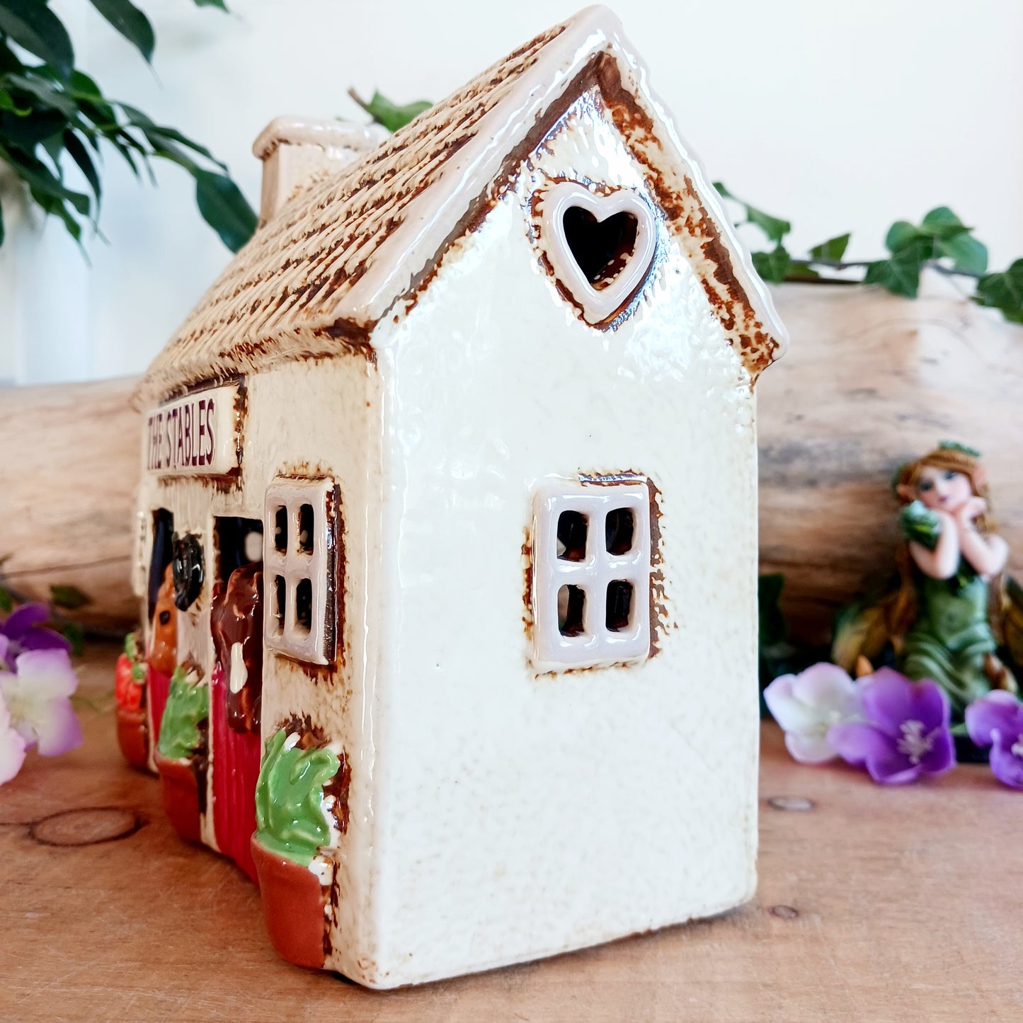 Nestled at the edge of a quiet enchanted village, The Stables tealight house by Village Pottery glows with a soft, grounding warmth. Crafted from ceramic and measuring 17x8x8cm, this rustic stable invites candlelight to flicker through its windows like a lantern for wandering spirits and kindred souls.