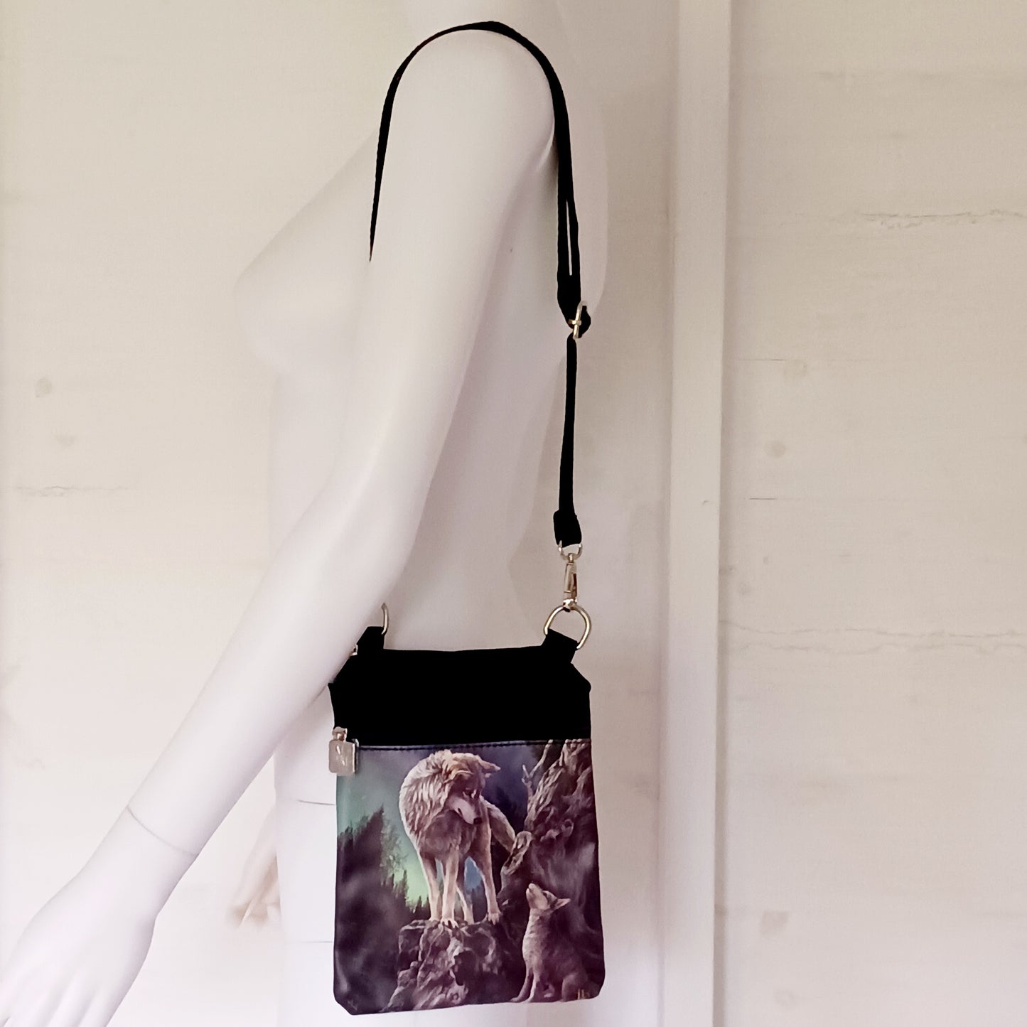 Step into a world of magic, guidance, and untamed wilderness with this stunning Lisa Parker Wolf & Pup Shoulder Bag, from Nemesis Now. Featuring enchanting artwork from the renowned fantasy and wildlife artist Lisa Parker, this bag captures a tender moment beneath a starlit sky as a majestic wolf watches protectively over their pup beneath the glowing aurora borealis.